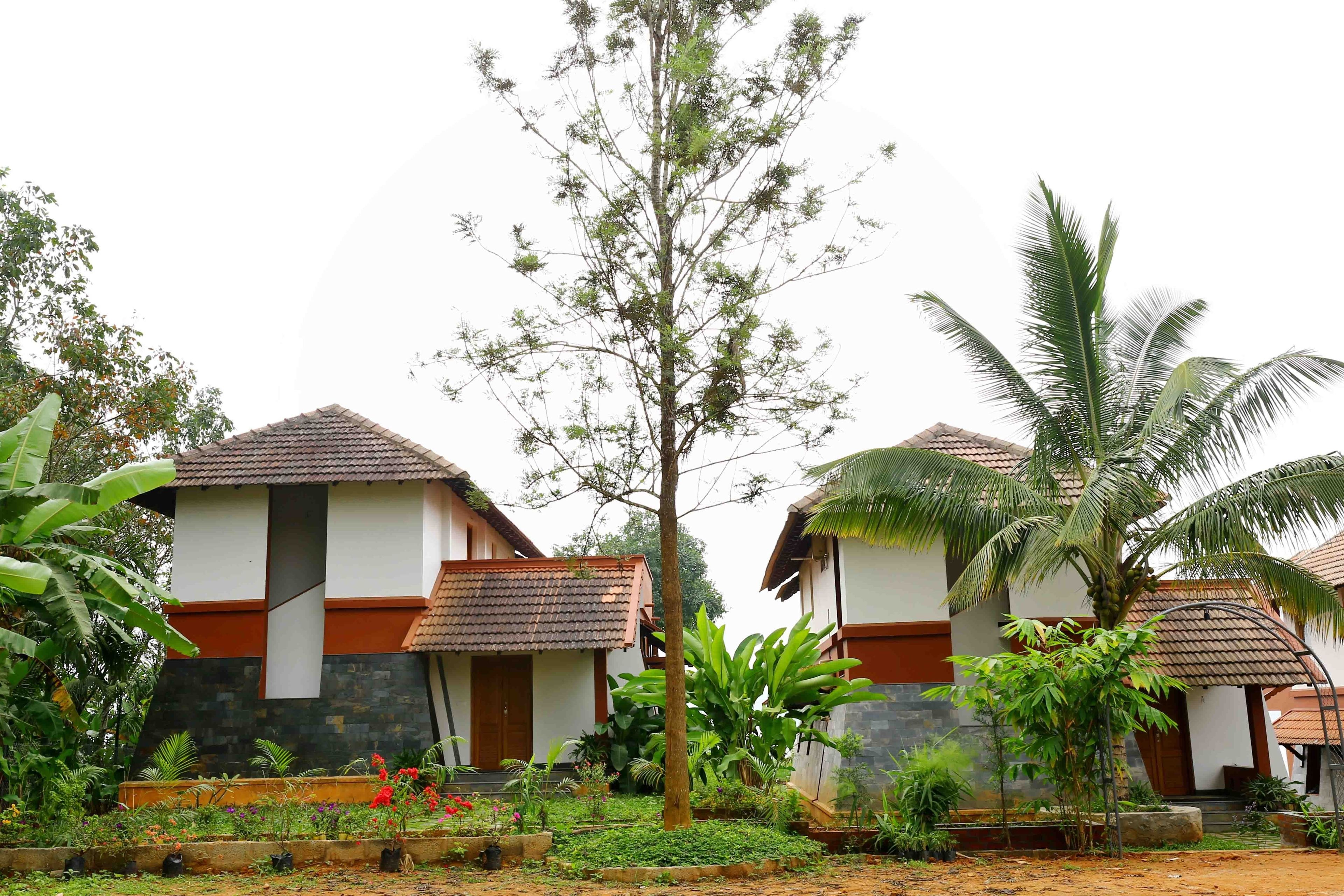 Un bâtiment de style bungalow, doté d’un toit en tuiles et d’une façade en pierre, entouré d’une végétation luxuriante et d’un jardin bien entretenu.