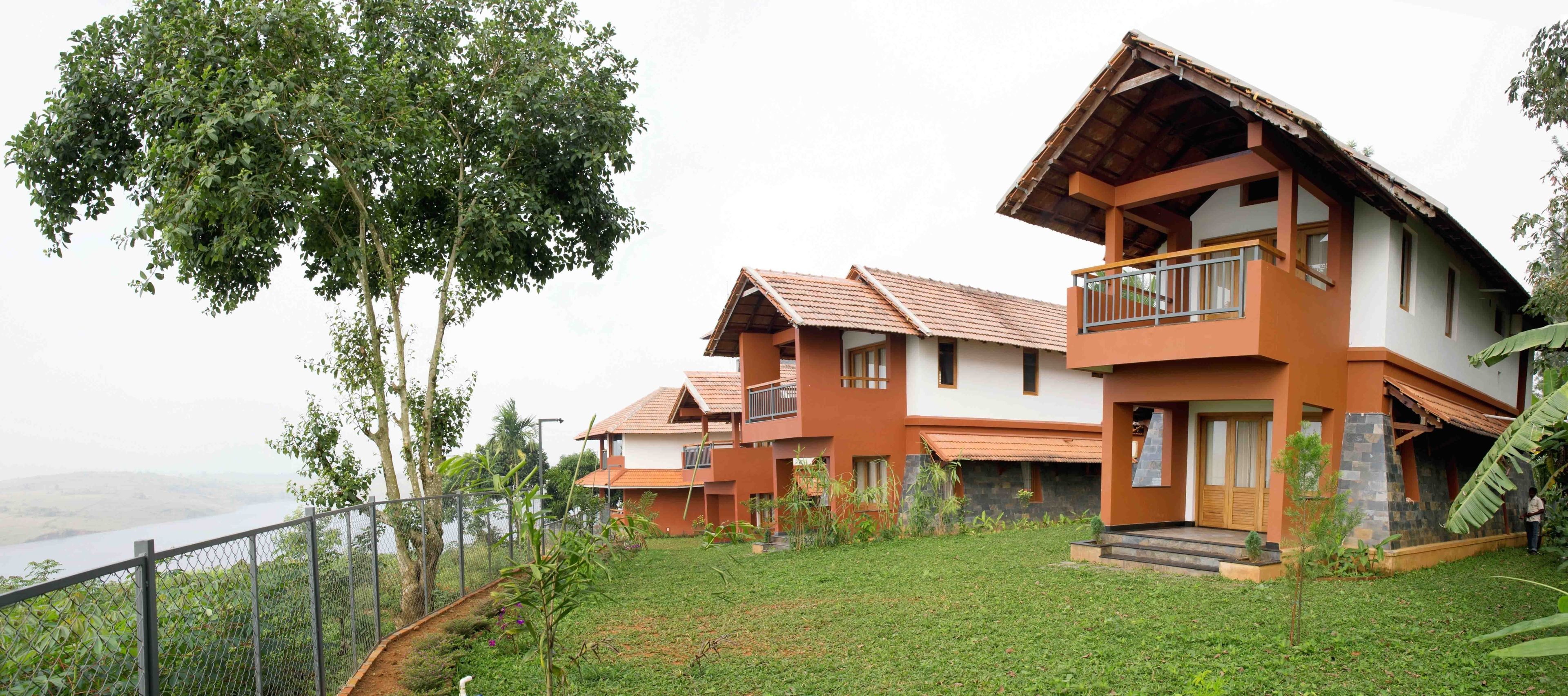 A modern two-story house with a balcony, surrounded by lush greenery and a view of a distant landscape.