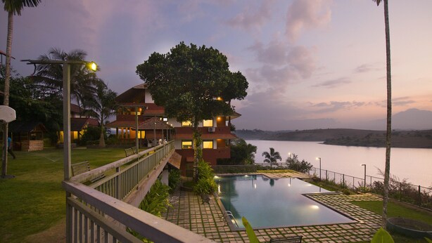 A resort with a swimming pool, a view of the lake, and a large tree in the foreground. - Vistara Resort (Sulthan Bathery)