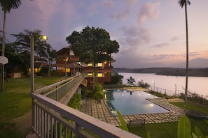 A resort with a swimming pool, a view of the lake, and a large tree in the foreground. - Vistara Resort (Sulthan Bathery)