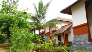 A courtyard with a stone pathway, lush greenery, and a row of buildings with red and white walls and tiled roofs. - Vistara Resort (Sulthan Bathery)