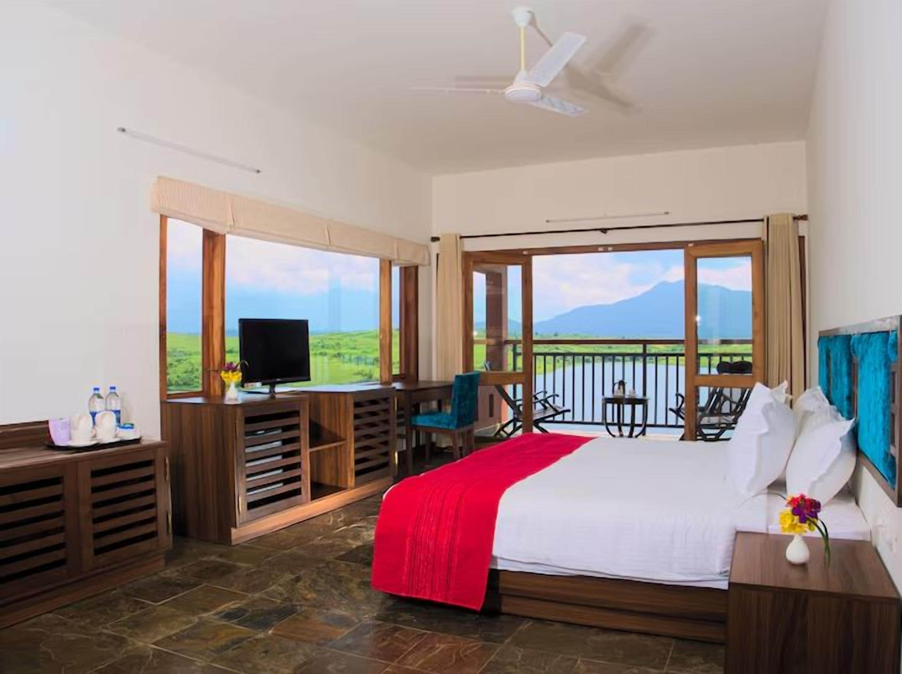 Ein Schlafzimmer mit einem großen Bett, einem Fernseher, einem Balkon mit Blick auf die Landschaft und einer Sitzecke mit Sesseln.