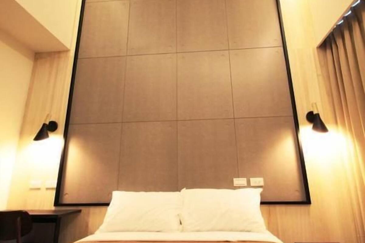 A hotel room with a large bed, two bedside tables, a wall-mounted light, and a curtain on the window.