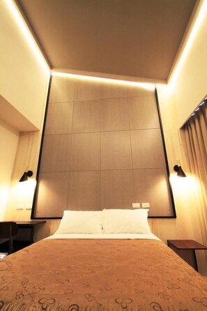 Quarto de hotel com uma cama grande, duas mesas de cabeceira, uma luminária na parede e cortina na janela.