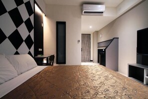 Quarto de hotel com uma cama grande, uma escrivaninha, uma cadeira e uma televisão.