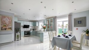 A modern kitchen with a central island, white cabinetry, and a dining area with a table set for two. - Amazing London (London)