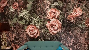 A teal sofa with two decorative pillows, set against a wall with a floral wallpaper design. - Amazing London (London)