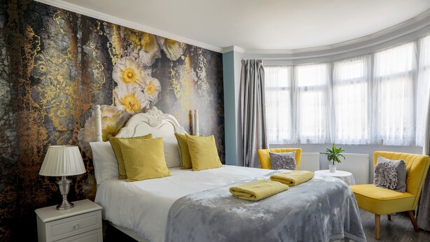 A bedroom with a large bed, a nightstand, a chair, and a window with curtains. - Amazing London (London)