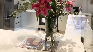 A modern kitchen with a white countertop, a stainless steel refrigerator, and a vase with pink flowers. - Amazing London (London)