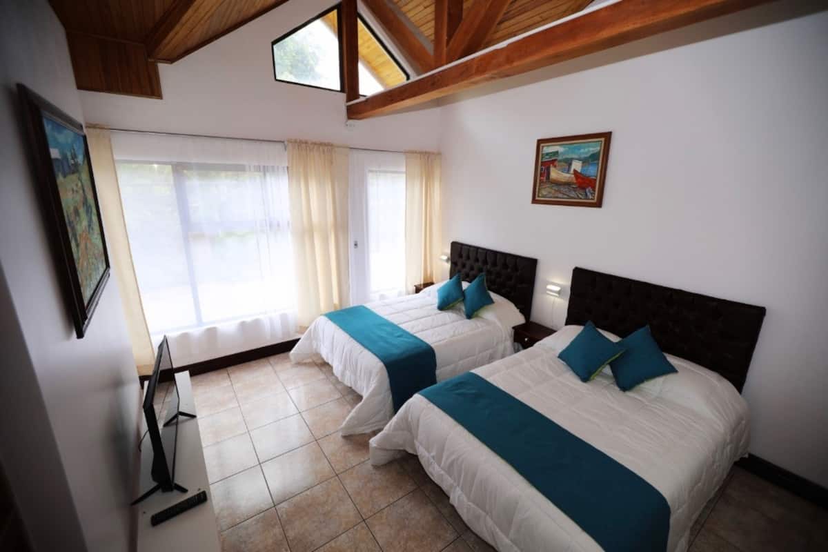 A hotel room with two beds, a painting on the wall, and a window with curtains.