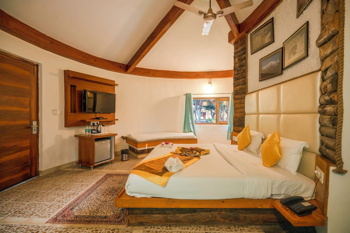 A hotel room with a large bed, a desk with a television, a stone accent wall, and a view of the outdoors.