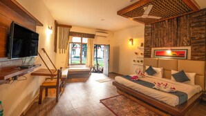 Una habitación de hotel moderna con techo de madera, televisor de pantalla plana, sofá cama, zona de comedor con mesa y sillas de madera, y vistas al exterior.