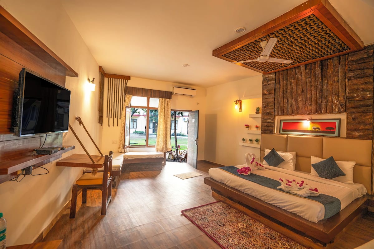 A modern hotel room with a wooden ceiling, a flat-screen TV, a sofa bed, a dining area with a wooden table and chairs, and a view of the outside.