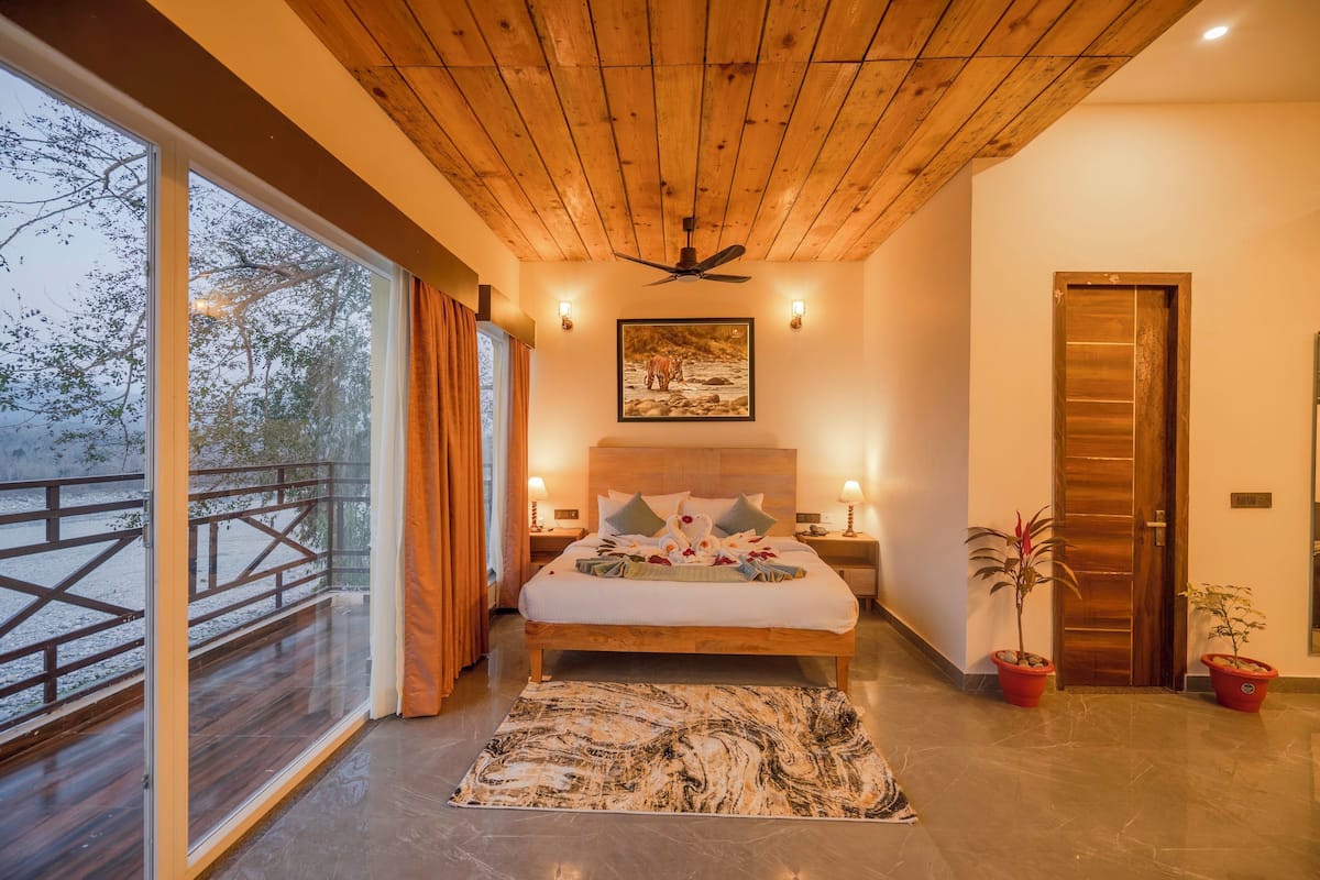 A bedroom with a large bed, wooden ceiling, and a view of a snowy landscape through a glass door.
