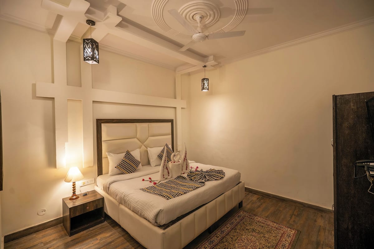 A bedroom with a large bed, a nightstand with a lamp, a ceiling fan, and a cross-shaped wall design.