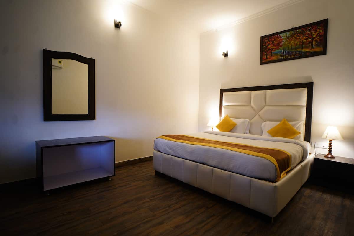 A hotel room with a bed, bedside table, lamp, and a painting on the wall.