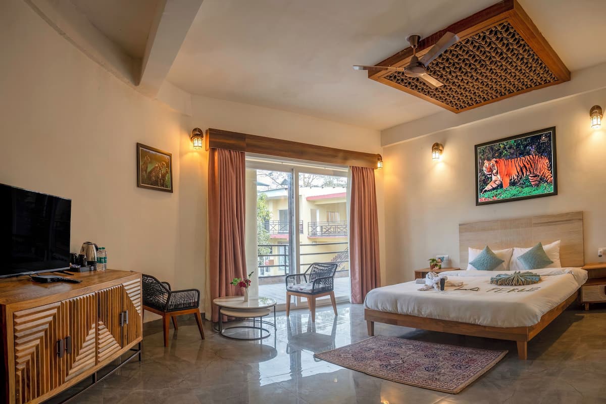 A hotel room with a bed, a TV, a wooden cabinet, a chair, a table, and a balcony with curtains.