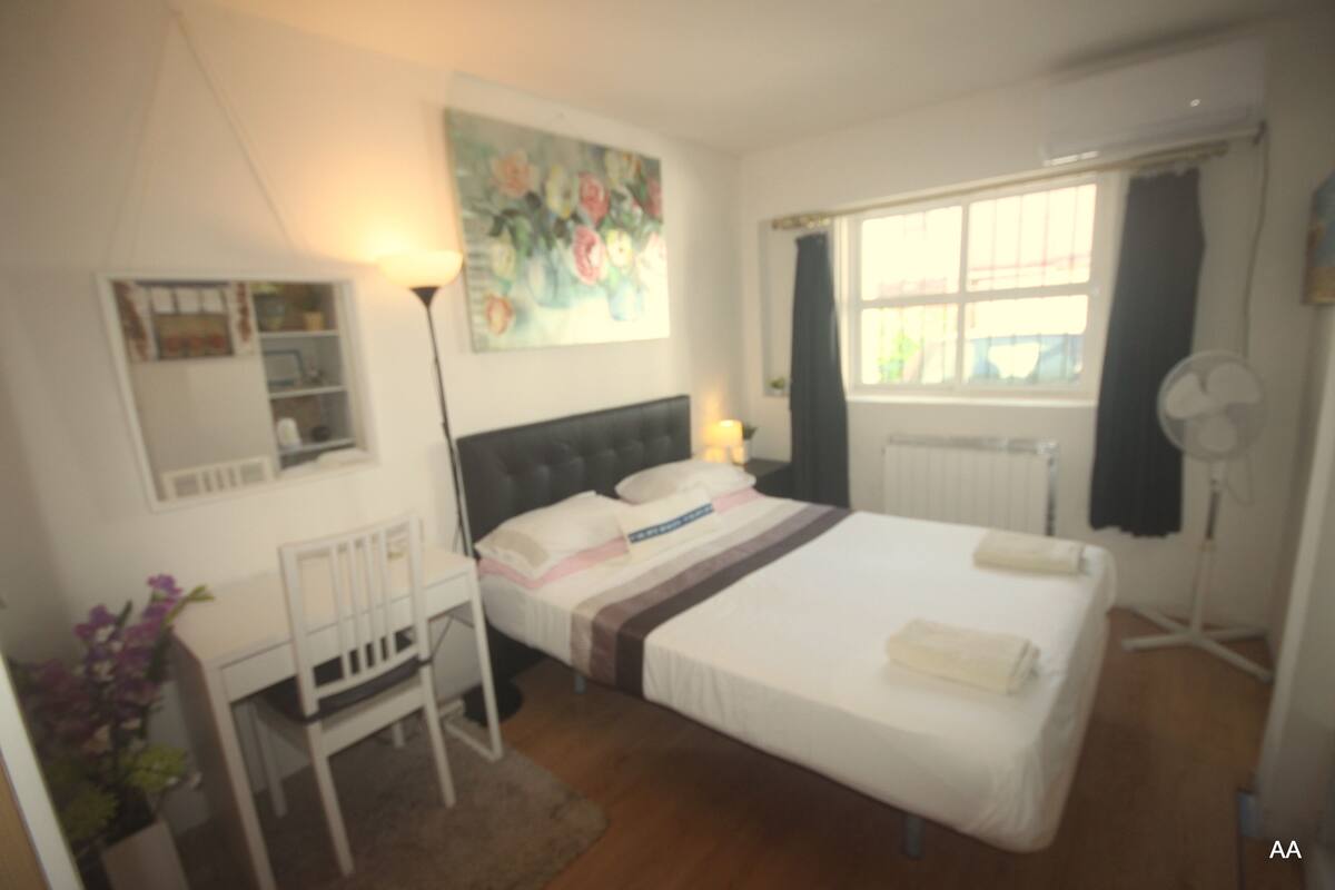 Ein Schlafzimmer mit Bett, Nachttisch, Stuhl und einem Fenster mit Vorhängen.