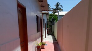 A narrow corridor with a red floor, potted plants, and a door on the left. - Hospedaje Mother Fanny (Puerto Villamil)