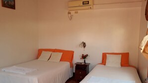 A hotel room with two beds, a nightstand, a wall-mounted air conditioner, and a small table with a vase of flowers. - Hospedaje Mother Fanny (Puerto Villamil)