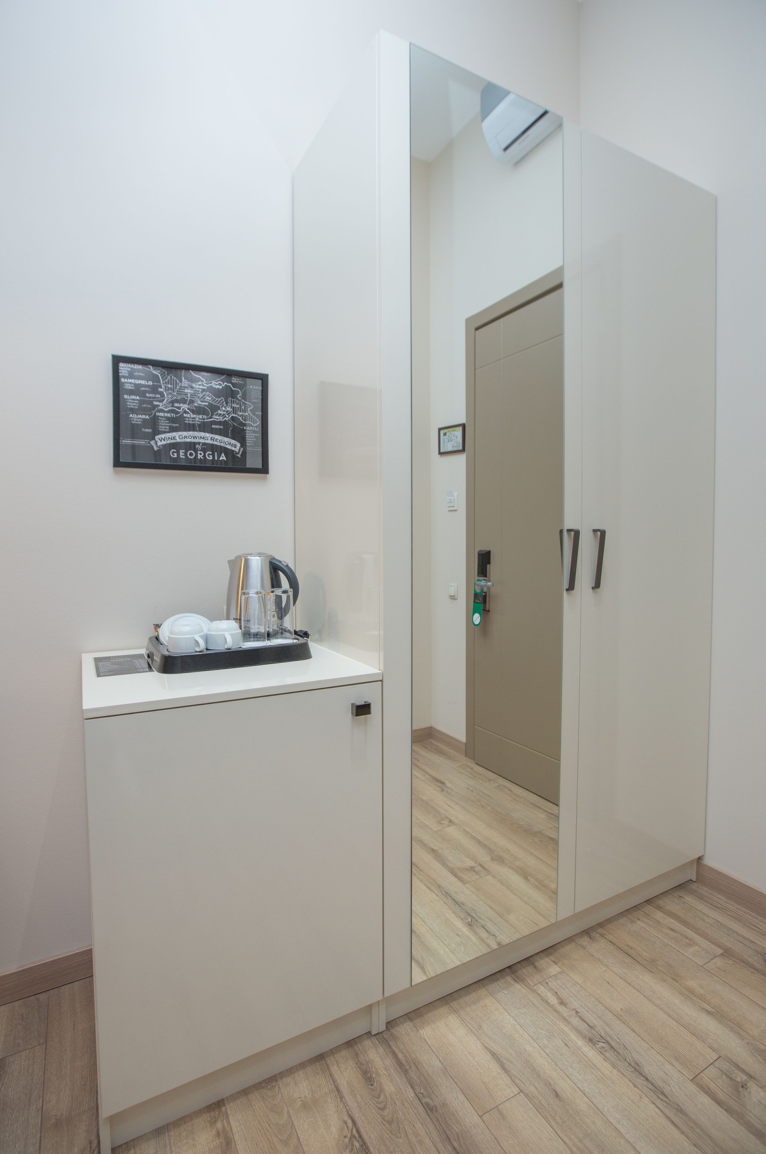 Quarto de hotel com um guarda-roupa branco, uma pequena mesa com uma cafeteira e um mapa emoldurado na parede.