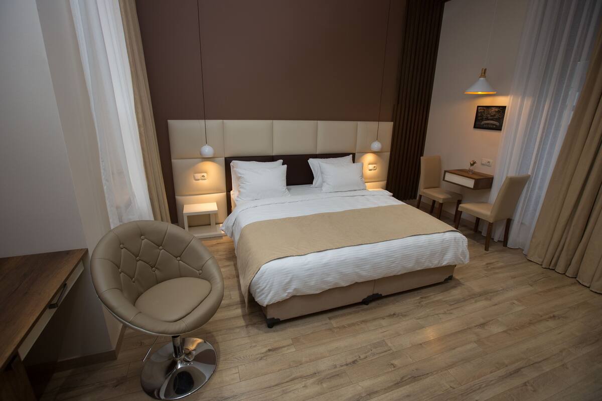 A modern hotel room with a large bed, a seating area with a chair, and a small table.