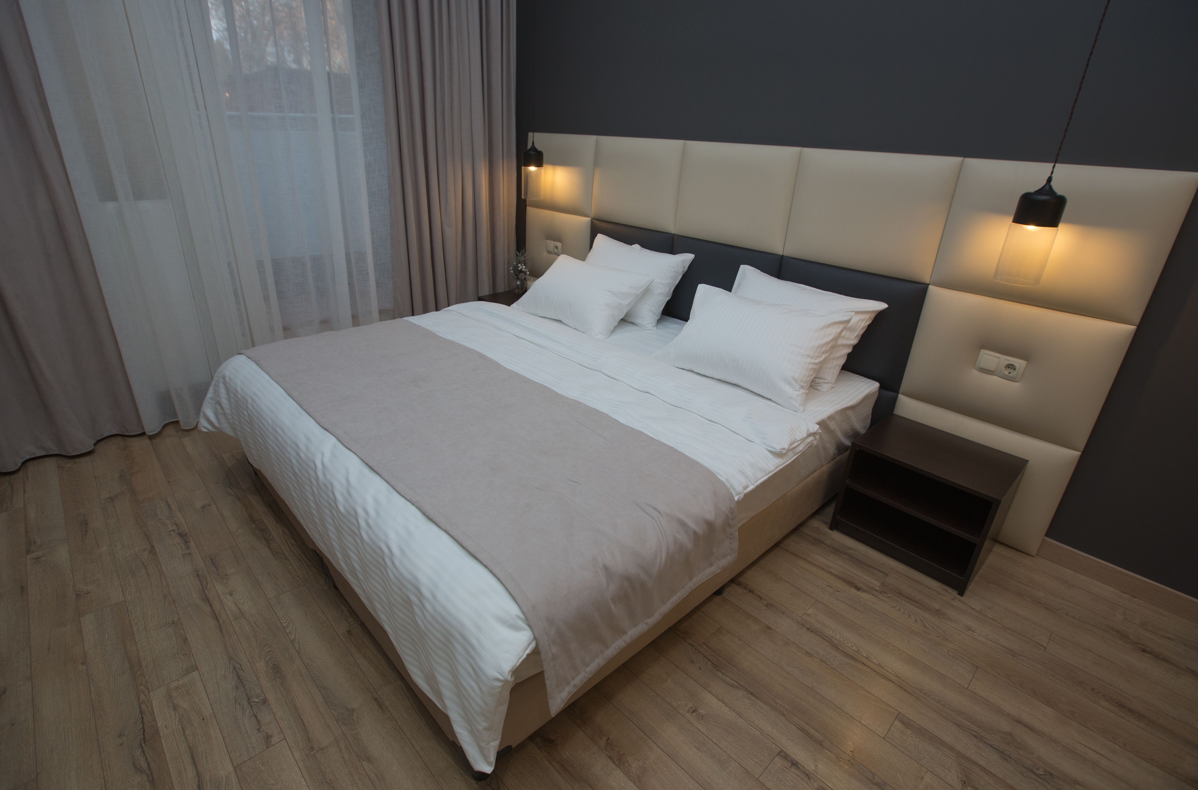 Quarto moderno com cama grande, piso de madeira e cabeceira com iluminação embutida.