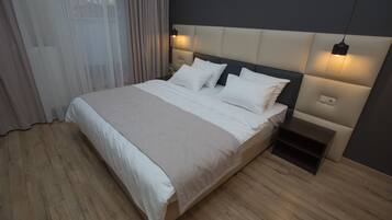 Quarto moderno com cama grande, piso de madeira e cabeceira com iluminação embutida.