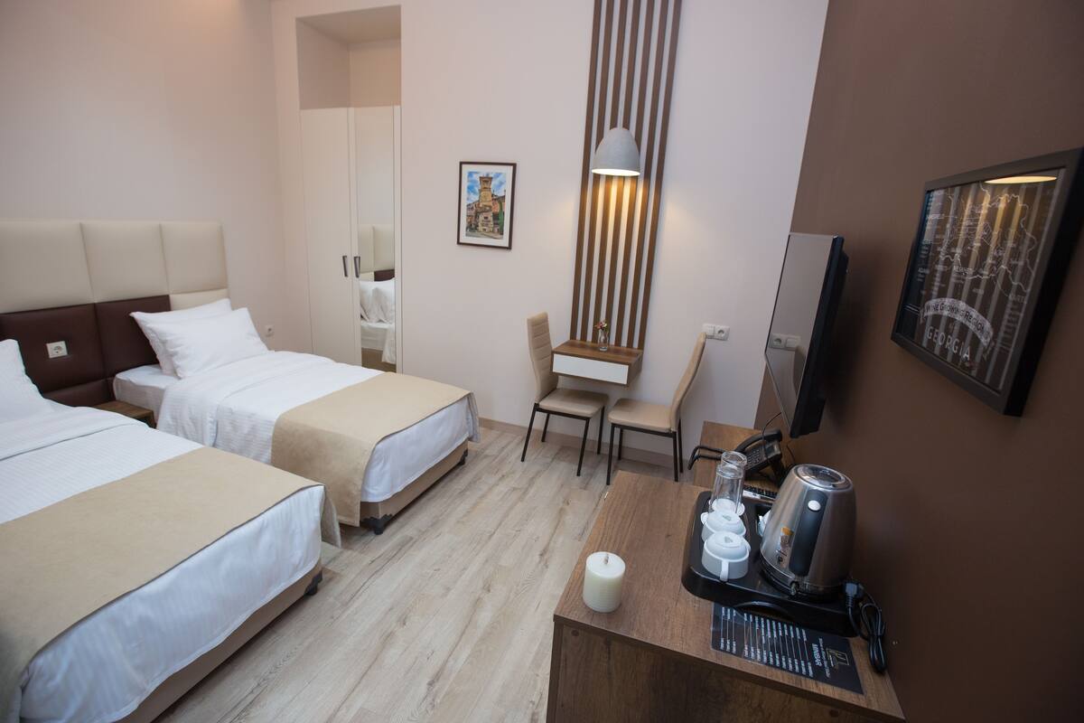 A hotel room with two beds, a desk with a lamp, a chair, a coffee maker, and a map on the wall.