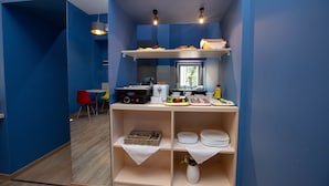 A modern kitchen with blue walls, a wooden floor, and a breakfast bar with plates, bowls, and a vase. - History Hotel Tbilisi (Tbilisi)