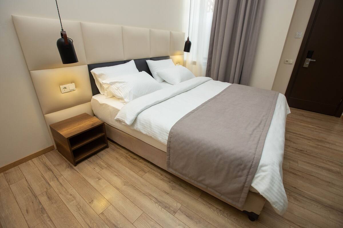 A neatly made bed with a headboard, bedside tables, and a hanging light fixture.