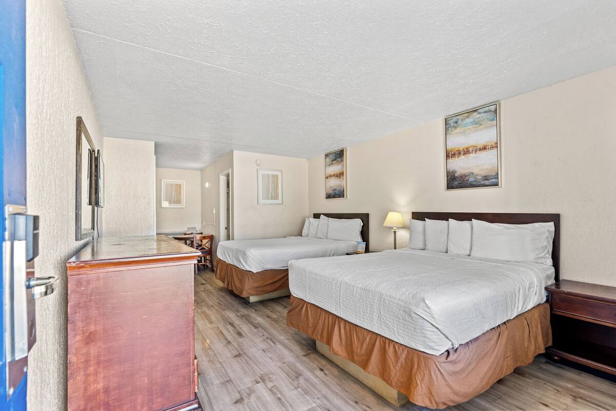 A hotel room with two beds, a wooden dresser, a desk, and a chair.