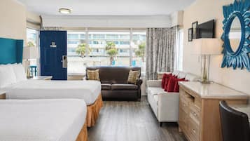 A hotel room with two beds, a sofa, a desk, and a view of the outside.