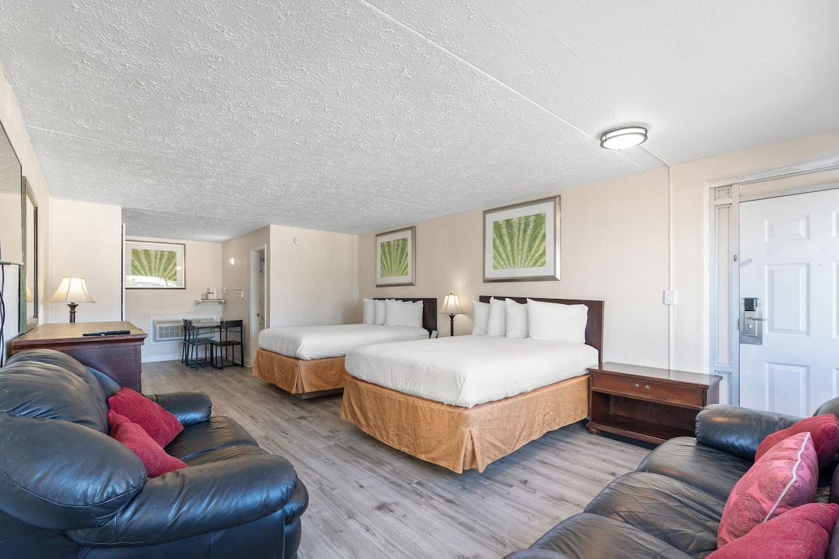 A hotel room with two beds, a sofa, a desk, and a chair.