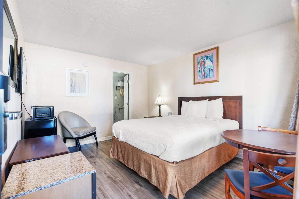 A hotel room with a bed, a desk, a chair, a lamp, and a painting on the wall.