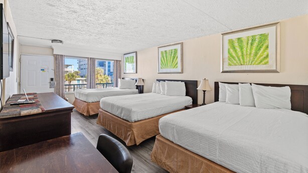 A hotel room with three beds, a desk, and a view of the city. - Ocean 5 Hotel (Myrtle Beach)
