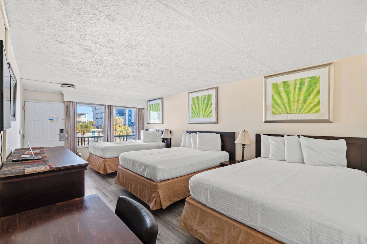 A hotel room with three beds, a desk, and a view of the city.