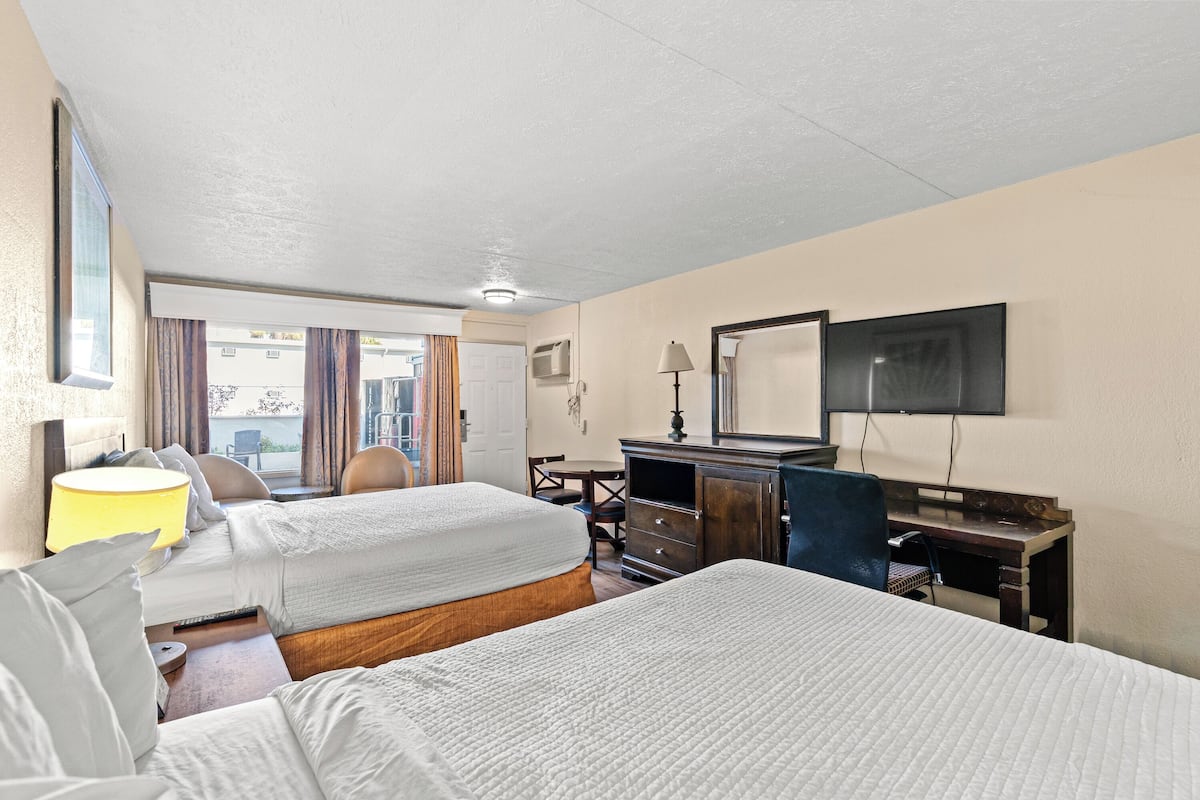 A hotel room with two beds, a desk, a chair, a TV, and a window.