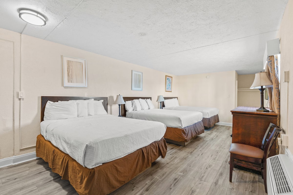 A hotel room with three beds, a desk, and a chair.