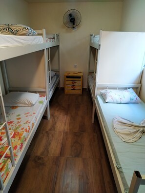 Un dormitorio con literas, un aparador de madera y un ventilador de pared.