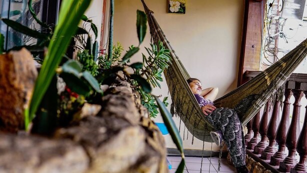 A person relaxing in a hammock indoors, surrounded by plants and wooden railings. - Hostel BH (Belo Horizonte)