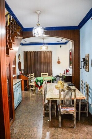 Un comedor con una mesa y sillas de madera, una araña y una escalera que sube a otra habitación.