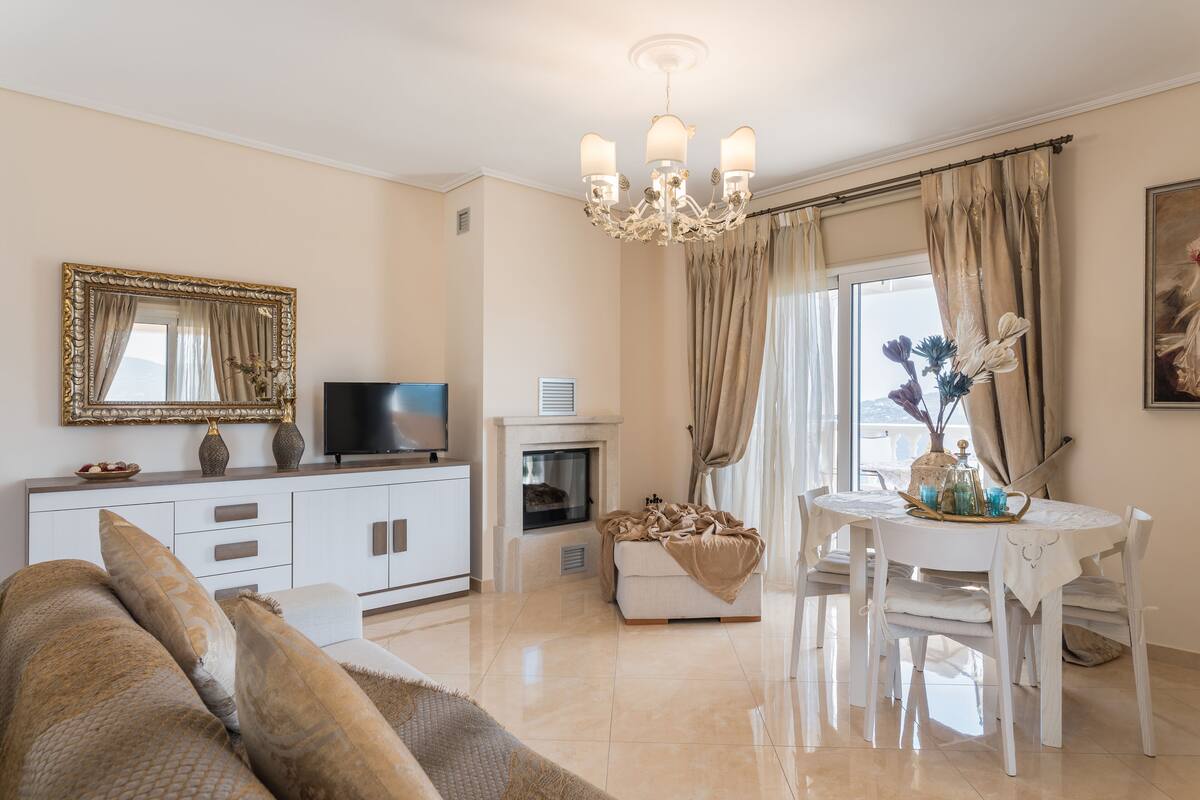 A living room with a sofa, TV, fireplace, dining table, and chandelier.