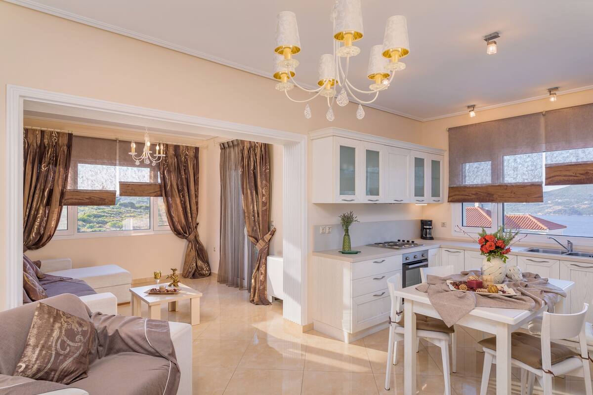 A modern living room with a sofa, a dining table with chairs, a kitchen area with cabinets, and a chandelier.