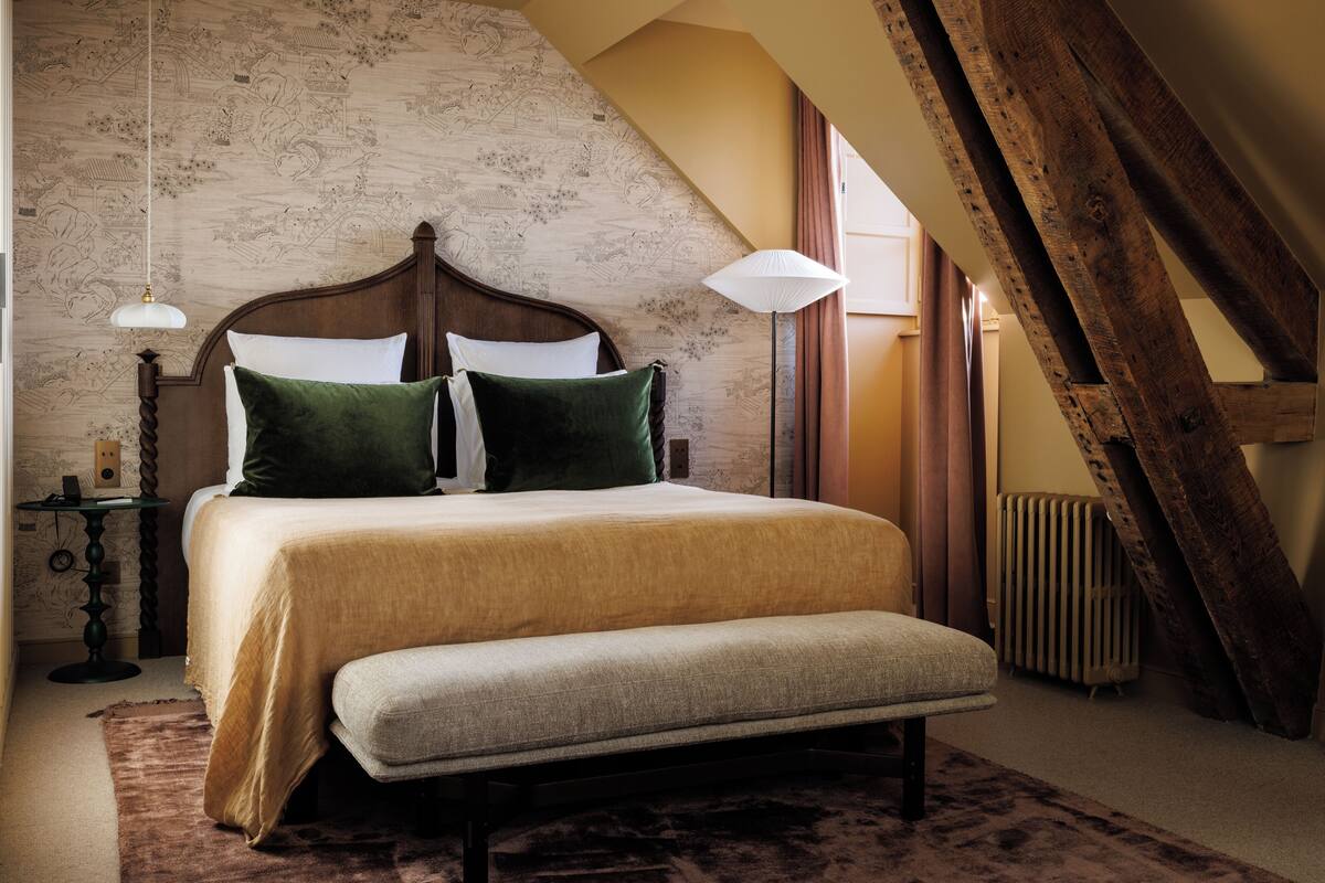 A bedroom with a large bed, a bench, a nightstand, a lamp, and a radiator.
