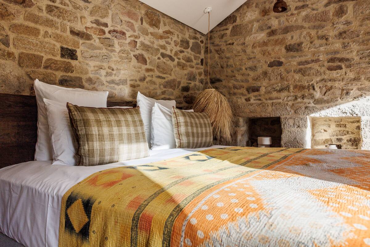 A stone-walled bedroom with a bed, pillows, and a blanket.
