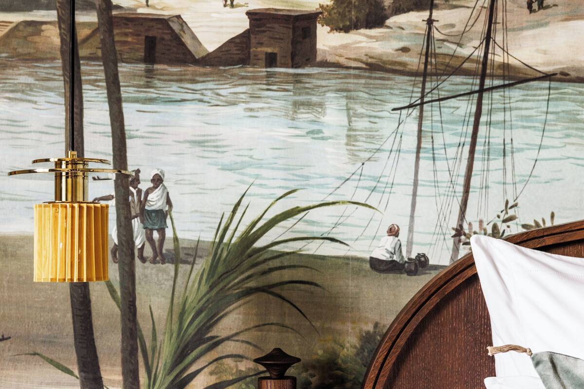 A room with a mural depicting a river scene, a wooden headboard, and a hanging lamp.