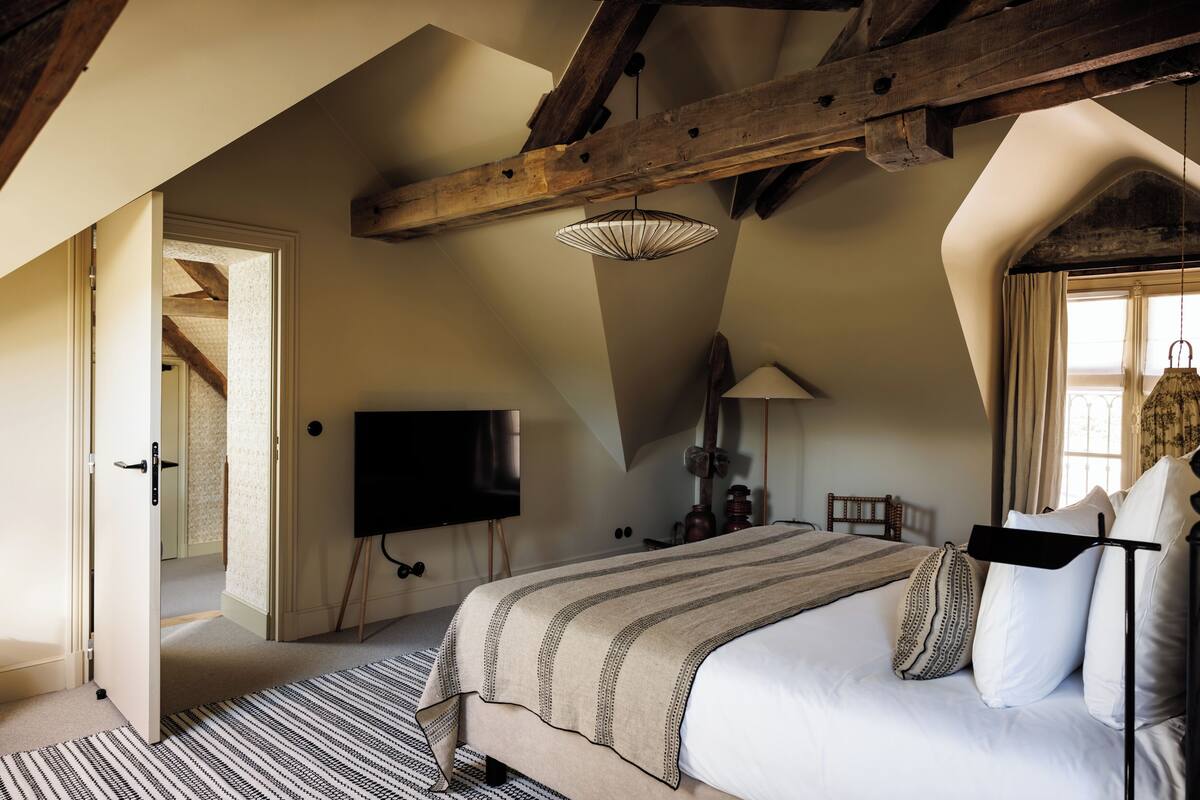 A bedroom with a large bed, a television, and a wooden ceiling beam.