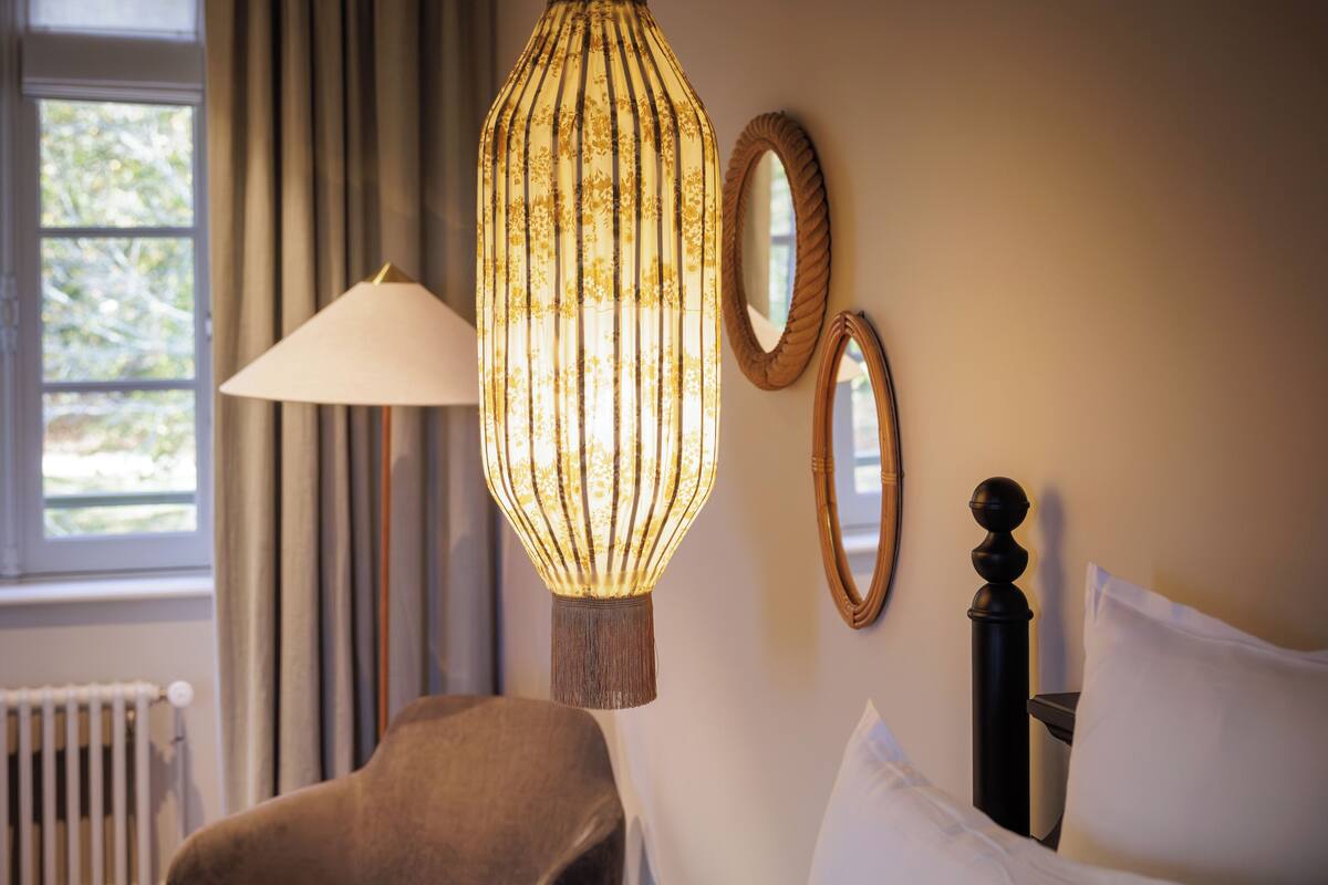 A room with a bed, a chair, a lamp, and two mirrors on the wall.