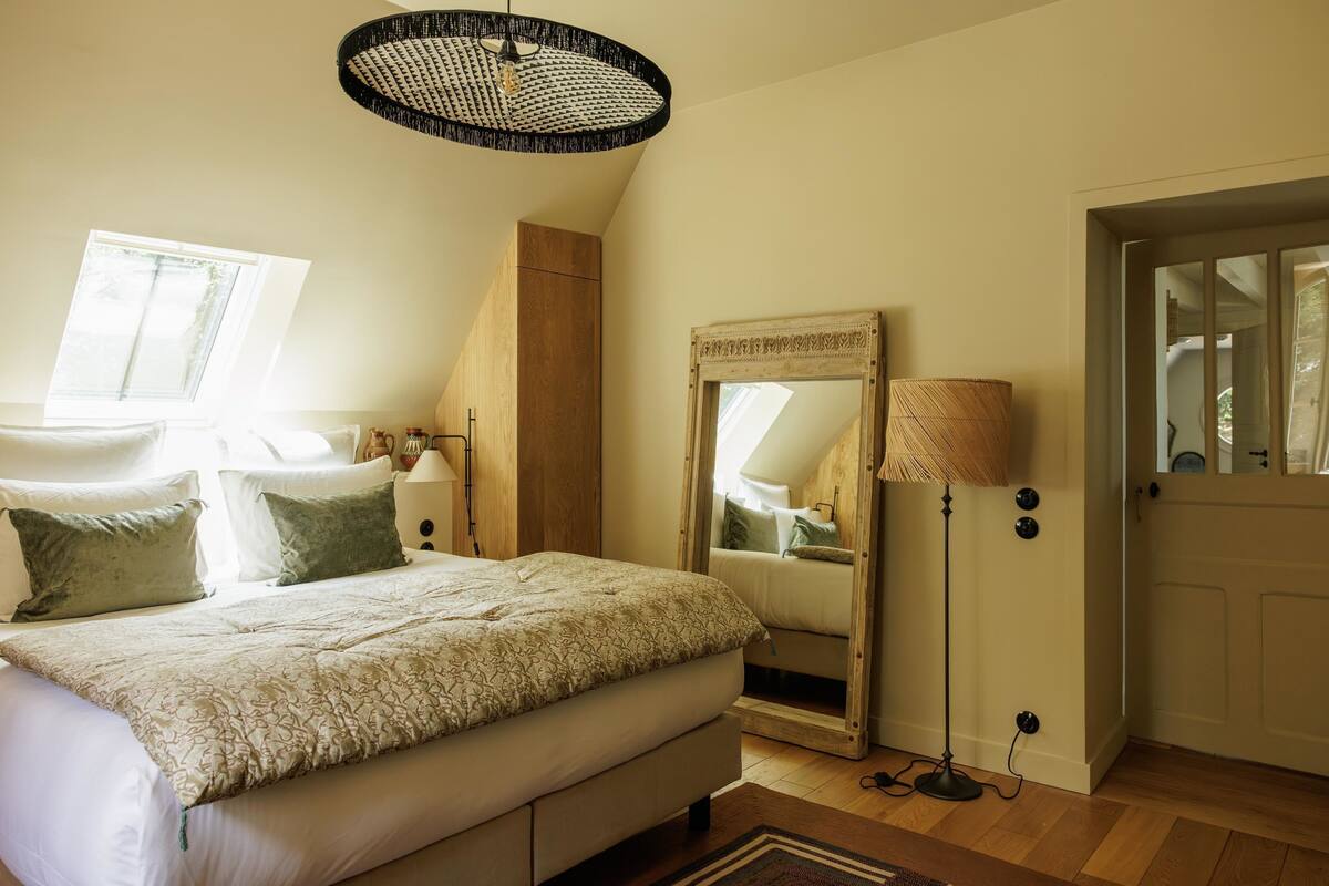 A bedroom with a large bed, a mirror, a floor lamp, and a door.